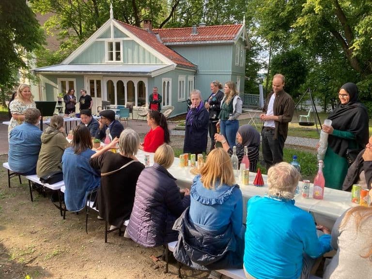 Naboer samlet rundt langbord i hagen utenfor et gammelt trehus