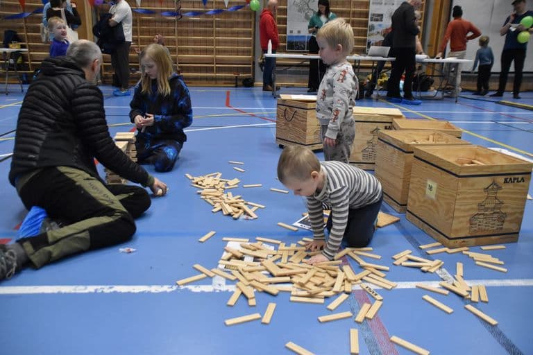 Barn og voksne bygger med treklosser på gulvet i hallen
