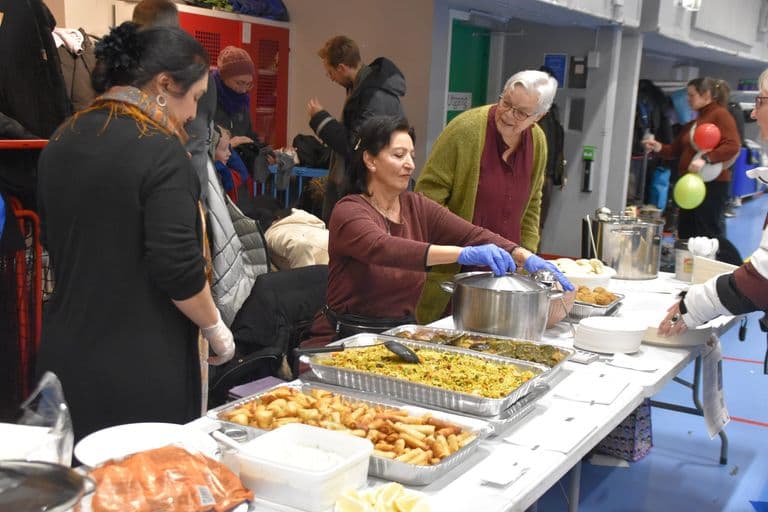 Frivillige serverer mat fra store brett på et langbord
