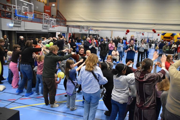 Barn og voksne leker ringlek med armene hevet i en full idrettshall