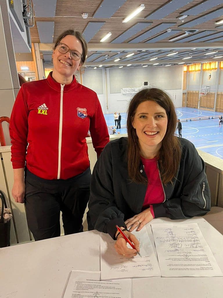 To smilende kvinner signerer samarbeidsavtalen på tribunen