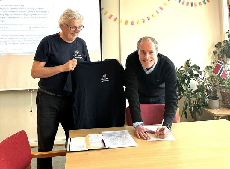 To menn signerer avtale og viser fram en t-skjorte