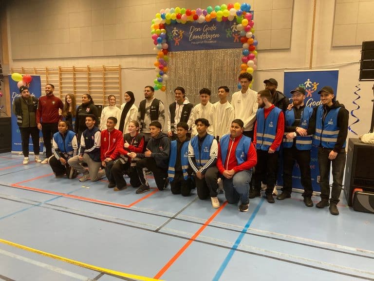 Ungdommer i blå vester samlet til gruppebilde foran scenen