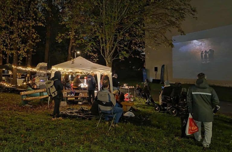 Film vist på en husvegg i mørket, med publikum i gresset