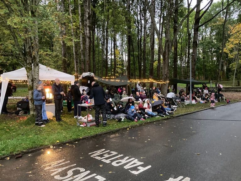 Publikum på tepper under trærne på utekino, med lysslynger over